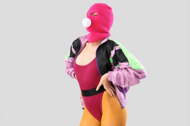 Kar maskeli, gri arka planda sakızı olan güzel, genç ve şık bir kadın.