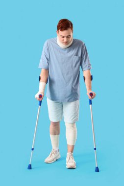 Mavi arka planda koltuk değnekleriyle kazadan sonra yaralanan genç adam.