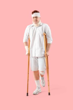 Pembe arka planda yürüyen koltuk değnekleriyle kazadan sonra yaralanan genç adam.