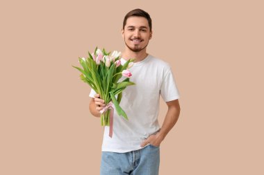 Bej arka planda güzel lalelerle dolu buketi olan mutlu genç bir adam. Uluslararası Kadınlar Günü
