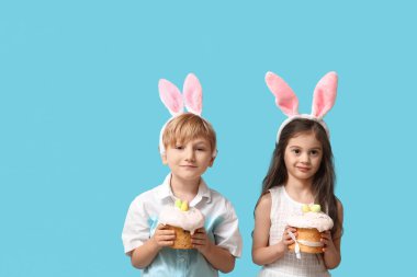 Mavi arka planda Paskalya pastaları olan tavşan kulaklı şirin çocuklar.