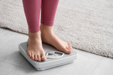 Evde terazinin üzerinde duran genç bir kadın. Kilo verme konsepti