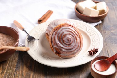 Tarçınlı çörekler ve ahşap arka planda malzemelerle dolu bir tabak.