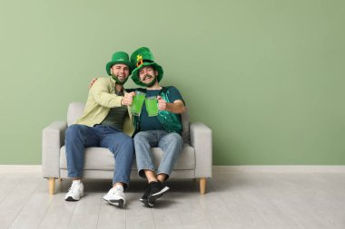 Yeşil sakallı, leprikon şapkalı genç adamlar ellerinde bira bardakları ve yeşil duvarın yanındaki kanepede oturuyorlar. Aziz Patrick Günü kutlaması