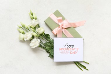 Mutlu Kadınlar Günü yazılı kart, hediye kutusu ve beyaz arka planda güzel östoma çiçekleri.