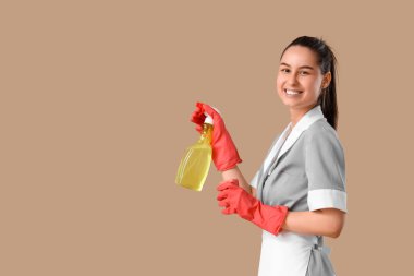 Kahverengi arka planda temizlik süngeri ve deterjanı olan genç oda hizmetçisi.