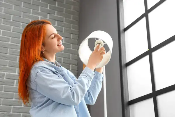 Pretty young woman changing light bulb in standard lamp at home