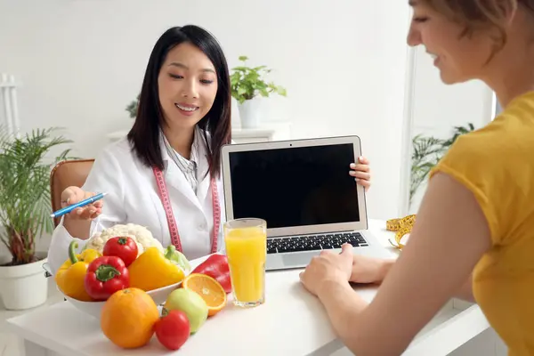 Female Asian nutritionist working with laptop and patient in office