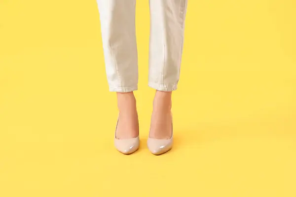 Legs of young woman in stylish beige high heels on yellow background