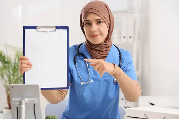 Female Muslim doctor pointing at clipboard in clinic
