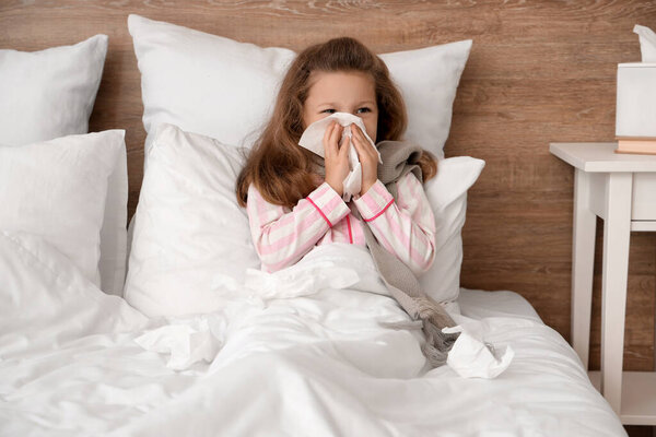 Sick little girl with tissue lying in bedroom