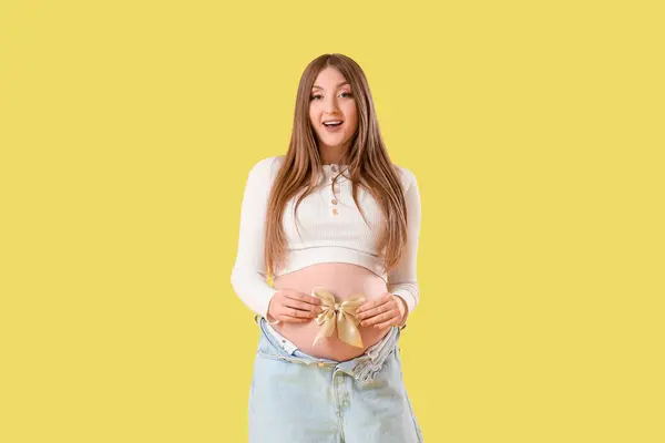 Young pregnant woman with bow on yellow background