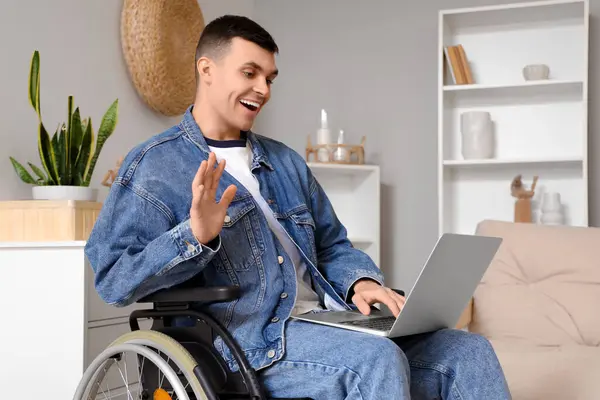 Happy young man in wheelchair with laptop video chatting at home