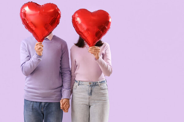 Young couple with heart-shaped balloons on lilac background. Valentine's Day celebration