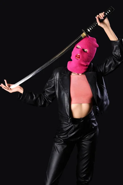 Beautiful young stylish woman in balaclava with sword on black background