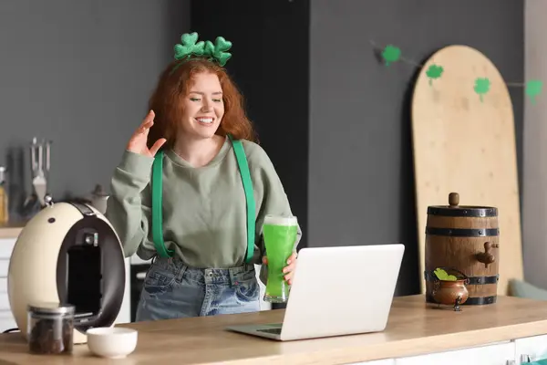 Young woman with beer and laptop in kitchen. St. Patrick\'s Day celebration