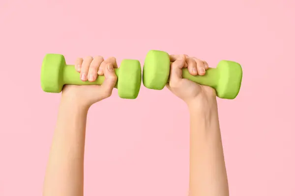 Female hands with green dumbbells on pink background, closeup