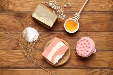 Saç derisi masaj aleti, şampuan çubukları ve kahverengi ahşap arka planda bir kase bal.