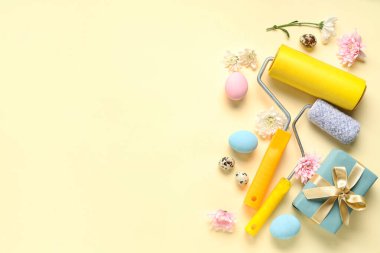Renkli arkaplanda boya ruloları, hediye kutusu, çiçekler ve Paskalya yumurtaları olan kompozisyon