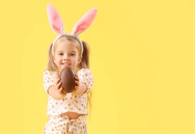 Sarı arka planda çikolatalı yumurtalı tavşan kulaklı şirin küçük kız.