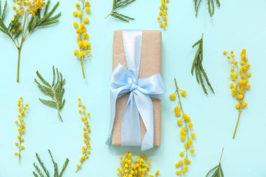 Mimoza çiçekli kompozisyon ve cyan arka planda paketlenmiş hediye kutusu