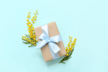 Cyan arka planda mimoza çiçekleriyle süslenmiş bir hediye kutusu.