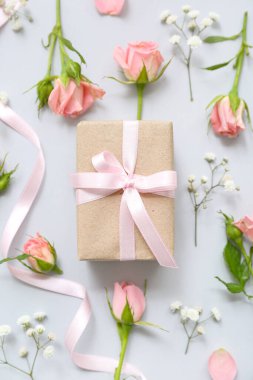 Açık arkaplanda gül çiçekleriyle süslenmiş güzel paketlenmiş hediye kutusu