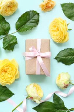 Cyan arka planda gül çiçekleriyle süslenmiş sevimli kağıt ambalajlı kompozisyon