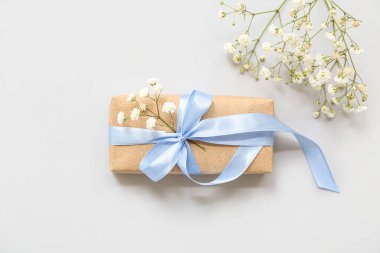 Işık arkaplanındaki çiçeklerle süslenmiş bir hediye kutusu.