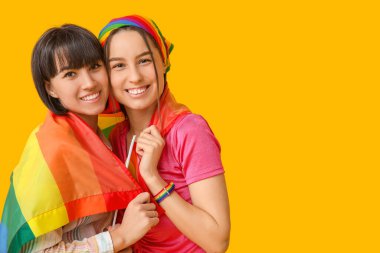 Sarı arka planda LGBT bayrağı olan genç lezbiyen çift