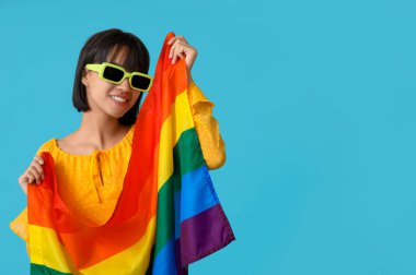 Mavi arka planda LGBT bayrağı olan güneş gözlüklü güzel bir kadın.