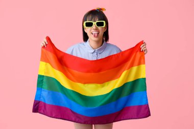 LGBT bayrağıyla pembe arka planda dilini gösteren güneş gözlüklü güzel bir genç kadın.