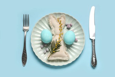 Mavi arka planda Paskalya yumurtası ve oyuncak tavşanı olan güzel bir masa.