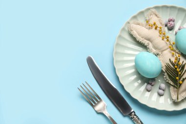 Mavi arka planda Paskalya yumurtası ve oyuncak tavşanı olan güzel bir masa.