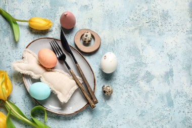 Paskalya yumurtaları, oyuncak tavşancık ve açık mavi arka planda sarı lalelerle güzel bir masa.
