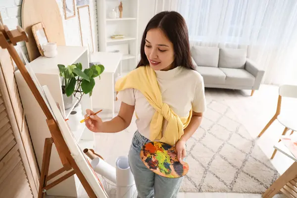 Female Asian artist drawing on canvas in workshop