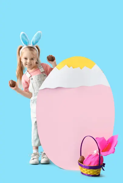 可爱的小女孩 长着兔子耳朵 戴着巧克力复活节彩蛋和蓝色背景的纸装饰 — 图库照片