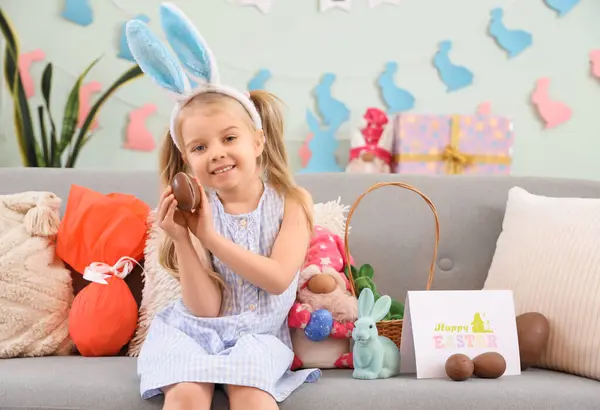 可爱的小女孩 长着小兔子耳朵 家里沙发上坐着巧克力复活节彩蛋 — 图库照片