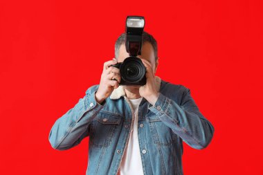 Kırmızı arka planda profesyonel kamerası olan olgun bir fotoğrafçı.