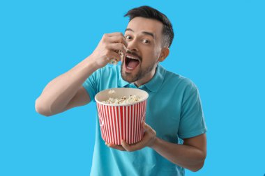 Yakışıklı adam mavi arka planda patlamış mısır yiyor.