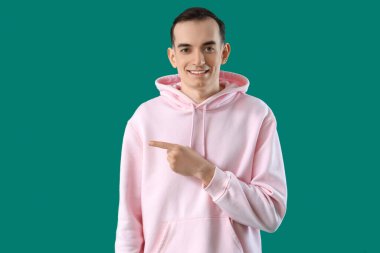 Genç adam yeşil arka plandaki bir şeyi işaret ediyor.