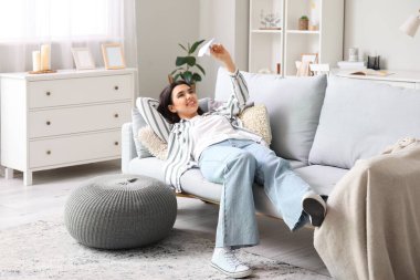 Evdeki kanepede kağıt uçakla yatan genç bir kadın.