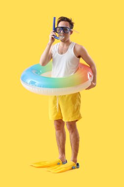 Sarı arka planda şnorkel maskeli ve yüzme yüzüklü genç adam.