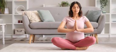 Sportif hamile kadın evde meditasyon yapıyor.