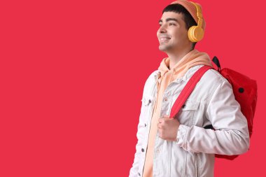 Kırmızı arka planda sırt çantalı kulaklıklı genç adam.