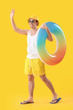 Sarı arka planda yüzme yüzüğü olan mutlu genç adam.