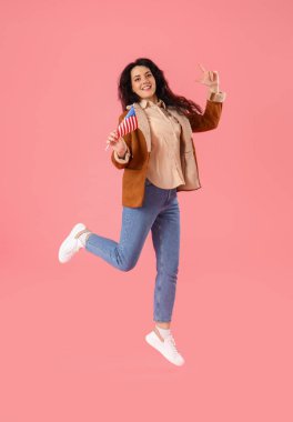 Pembe arka planda Amerikan bayrağı taşıyan kaygısız atlayan genç kadın.