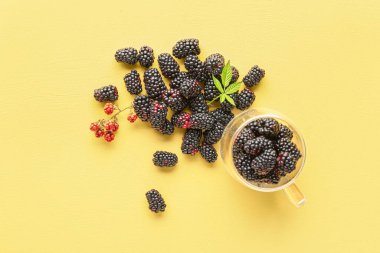 Sarı arka planda taze böğürtlenli cam bardak.