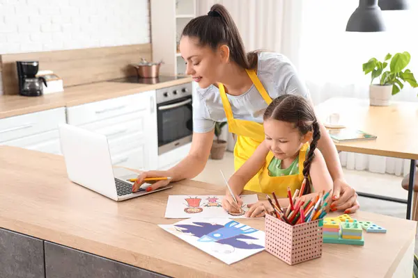 Little girl with her working mother drawing in kitchen