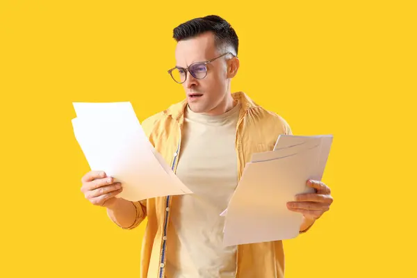 Stressed young man with papers on yellow background. Deadline concept